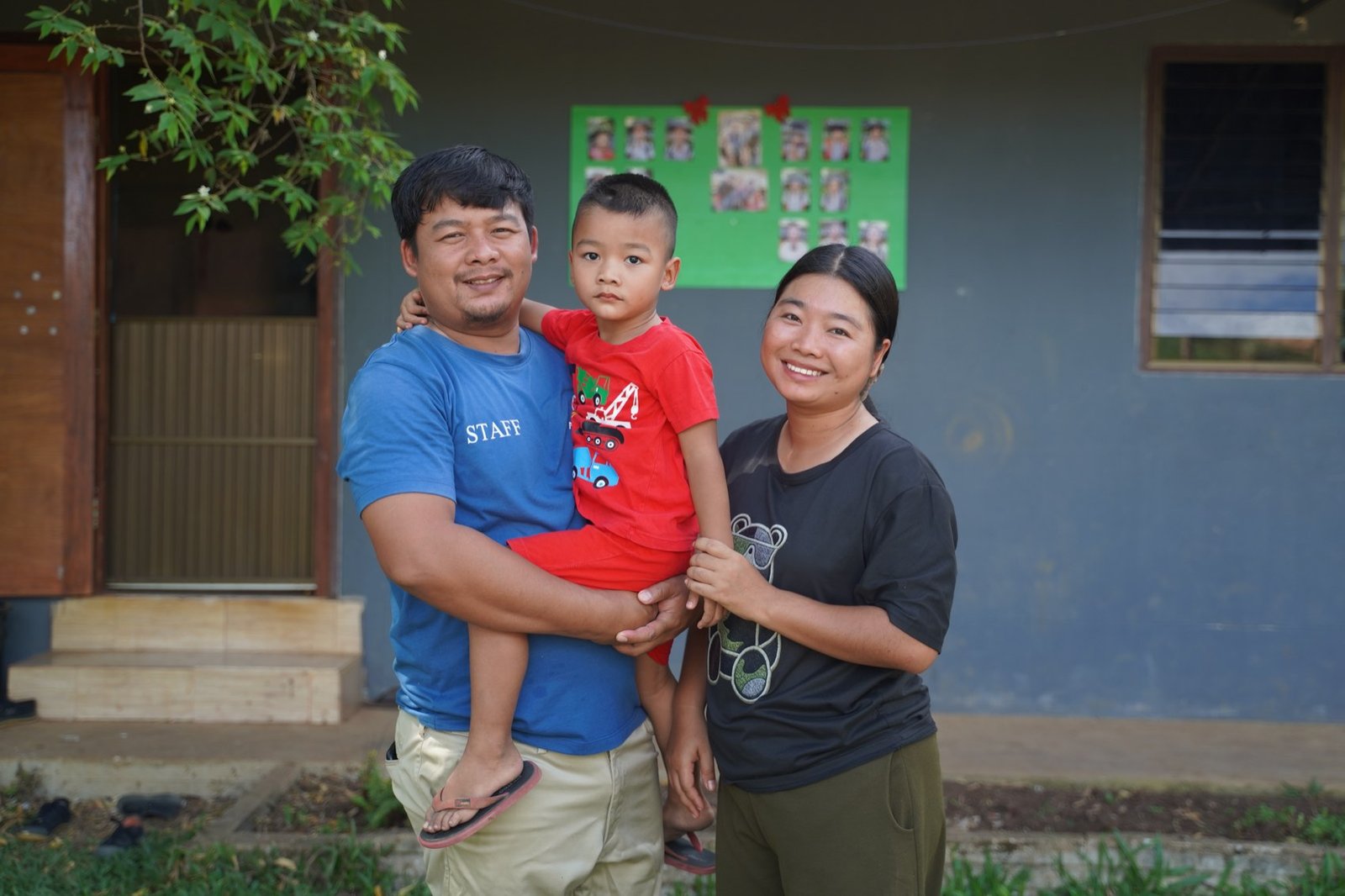 House parents holding a young boy outside their Kinship home